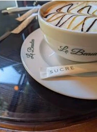 Une vraie tasse de café et sa soucoupe marquée Le Beaulieu, posées sur une table